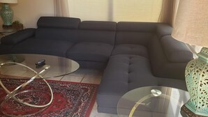 Olohuoneessa on tumma sohva, lasinen sohvapöytä, punakuvioinen matto ja koristeellinen lamppu.