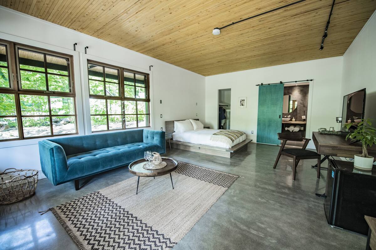 A modern living room with a blue sofa, a wooden coffee table, and a large window with a view of greenery.