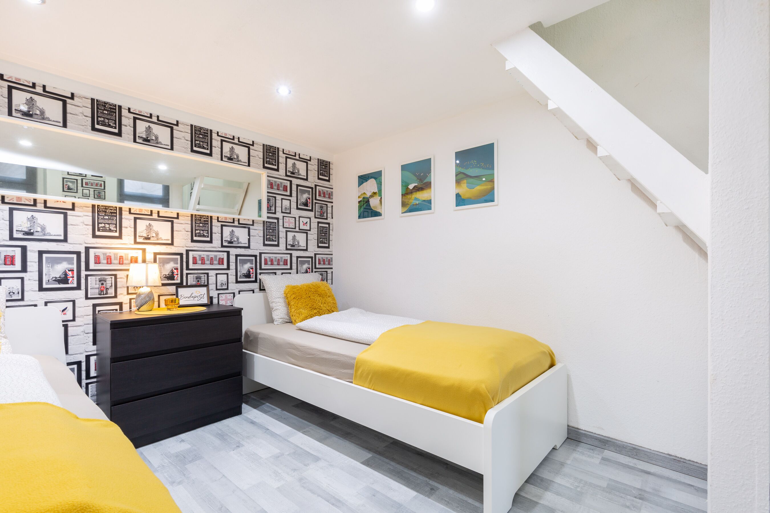 A bedroom with a bed, a dresser, a mirror, and a wall decorated with framed pictures.