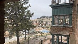 A view from a balcony overlooking a town with a mix of residential and commercial buildings, a clear sky, and a prominent tree in the foreground. - Hotel St. Nicholas (Cripple Creek)