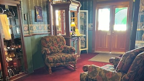 A room with a red carpet, a floral armchair, a wooden cabinet, and a mirror. - Hotel St. Nicholas (Cripple Creek)