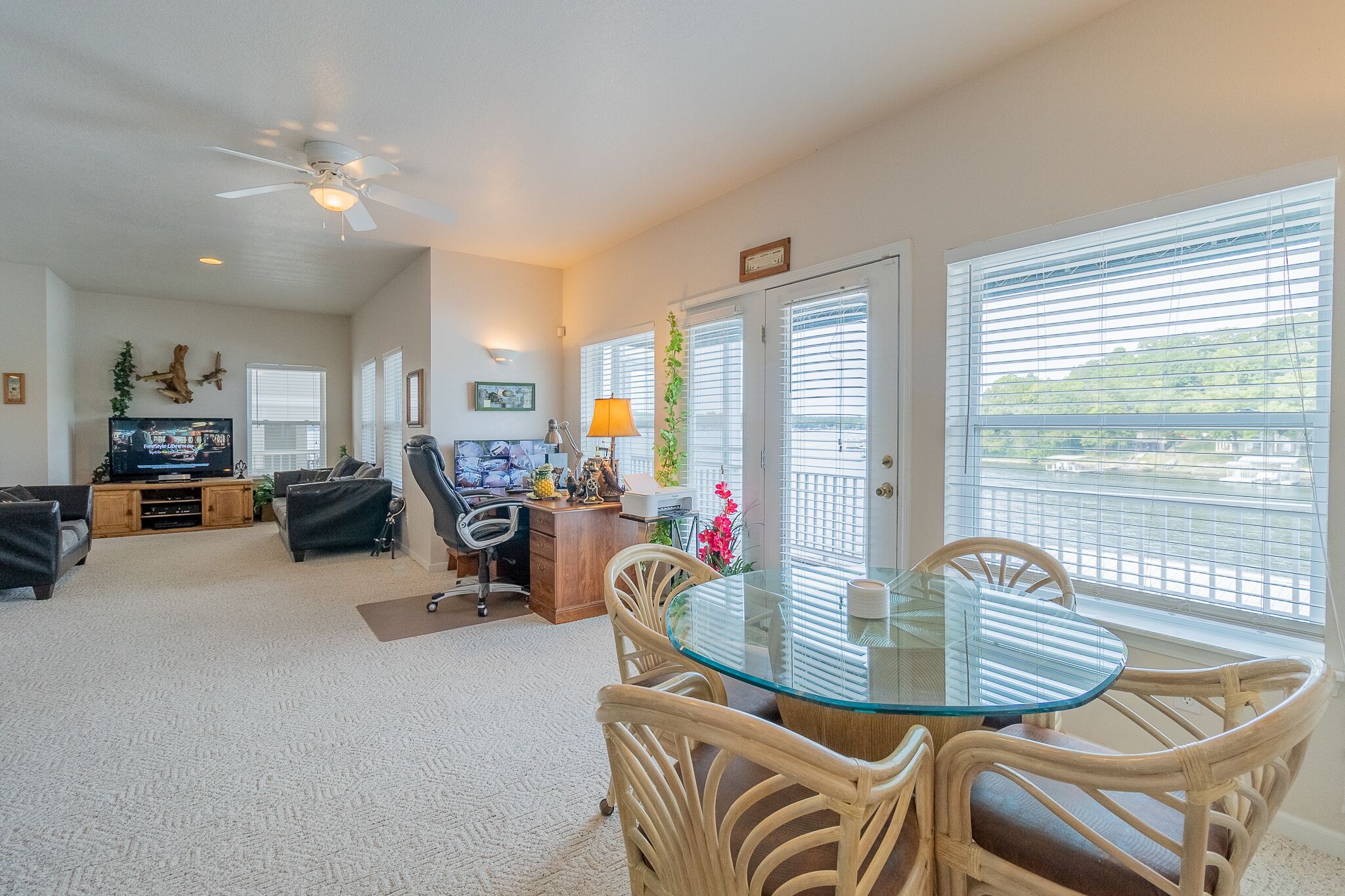 A spacious living room with a glass-top dining table, comfortable seating, a TV, and a ceiling fan.