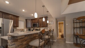 A kitchen with a stone island, bar stools, stainless steel appliances, and pendant lighting. - Falls 90 - Beautiful 3 Bdrm Falls Condo (Lake Ozark)