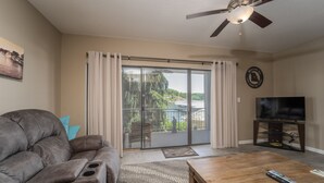 A living room with a gray sofa, a wooden coffee table, a TV on a stand, and a ceiling fan. - Falls 90 - Beautiful 3 Bdrm Falls Condo (Lake Ozark)