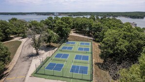 A tennis court surrounded by trees and a lake. - Regatta Bay 488 - Walk In 3 Bdrm Condo (Village of Four Seasons)