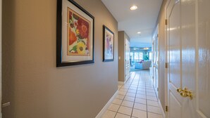 A hallway with framed floral artwork on the walls, a tiled floor, and a door with a gold handle. - Falls 118 - 4 Bdrm condo with Breathtaking View (Lake Ozark)