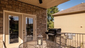 Une terrasse couverte avec un mur en pierre, un barbecue et une table ronde en métal, accompagnée de chaises.