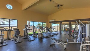 Une salle de sport spacieuse, dotée de divers appareils d’exercice, de grandes fenêtres et offrant une vue sur des palmiers.