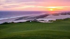 Un parcours de golf avec un mât de drapeau, une vue sur l’océan et un coucher de soleil.
