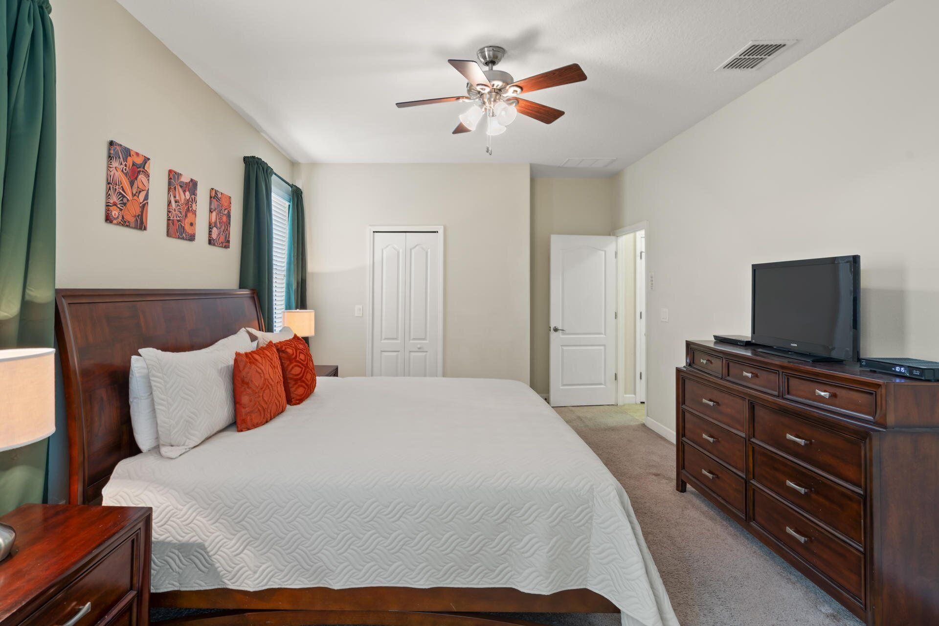 A bedroom with a bed, a dresser, a ceiling fan, and a television.