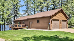A wooden cabin with a deck, garage, and a view of a lake.