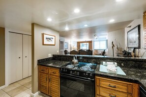Uma cozinha com fogão preto, armários de madeira e chão de azulejos.