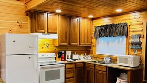A compact kitchen with wooden cabinets, a refrigerator, stove, microwave, and a sink.