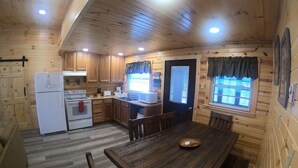 A cozy cabin-style kitchen with wooden walls and ceiling, equipped with a refrigerator, stove, and sink.