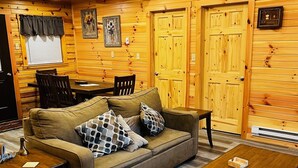A cozy cabin interior with a sofa, two armchairs, a coffee table, and a dining table.