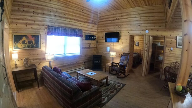 A cozy cabin interior with a wooden ceiling, a sofa, a table, a rocking chair, a TV, and a window with blinds. - Ugly Cabin, Stunning Escape – Hot Tub! Fire Pit! Fast WIFI! Sunroom! Hiking! (Elkins)