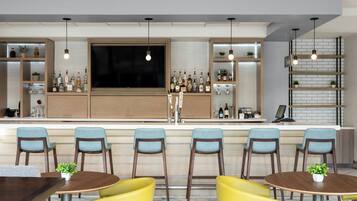 A bar area with multiple seating options, including bar stools and round tables, with a variety of bottles and glasses on shelves.