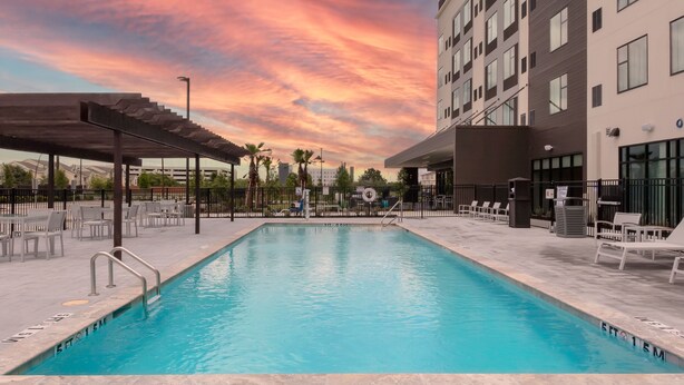 Ein Swimmingpool mit Sonnenuntergangshimmel, umgeben von Liegestühlen und einem überdachten Bereich.