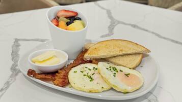 A breakfast plate with eggs, bacon, toast, butter, and a fruit cup.