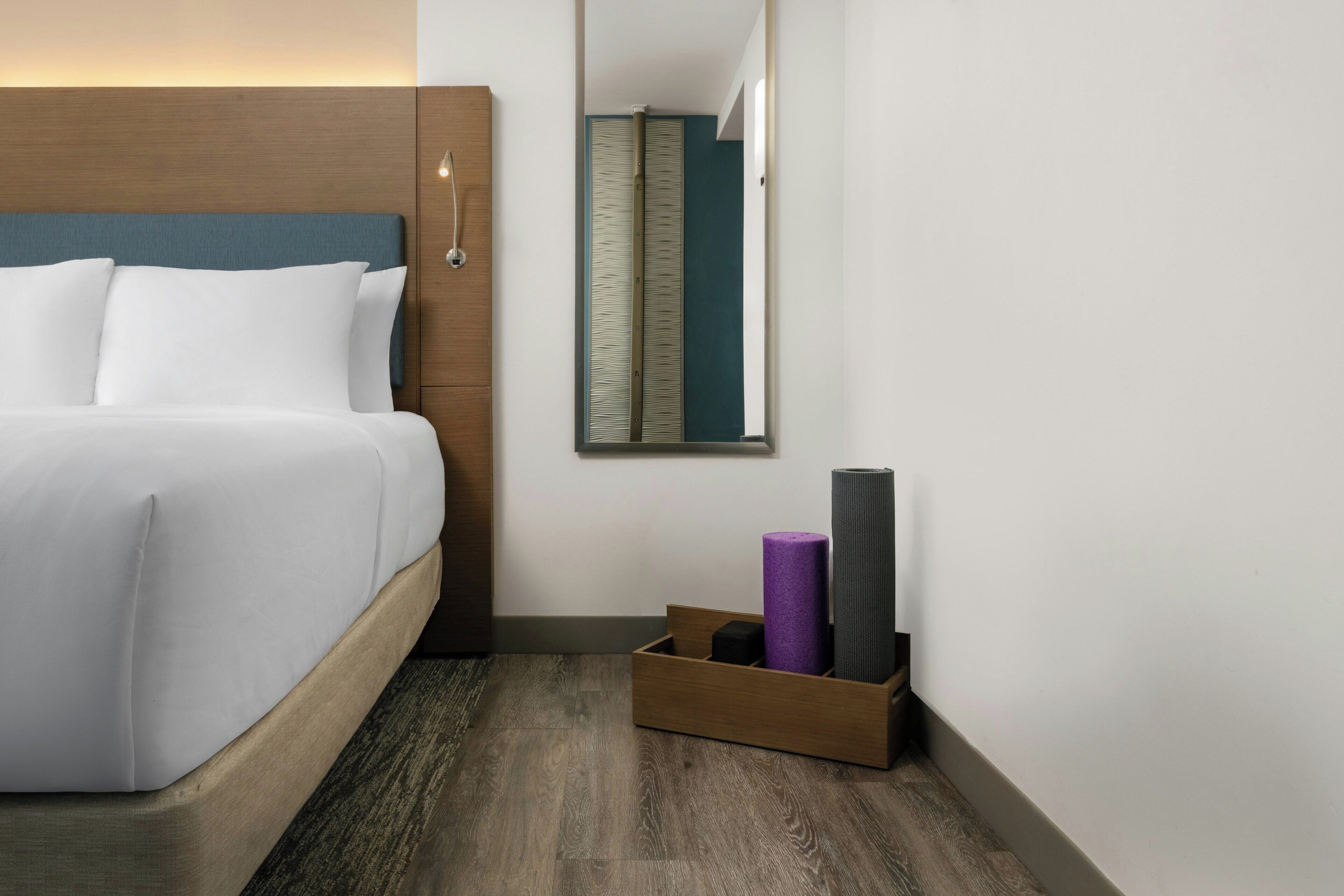 A hotel room with a bed, a mirror, a wooden headboard, a small wooden box with items, and a patterned wall.