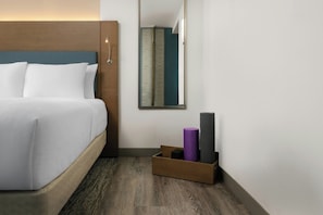 Habitación de hotel con cama, espejo, cabecero de madera, una pequeña caja de madera con objetos y pared estampada.