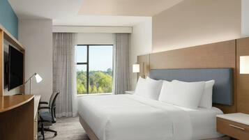 A hotel room with a large bed, a desk, a chair, a television, and a window with curtains.