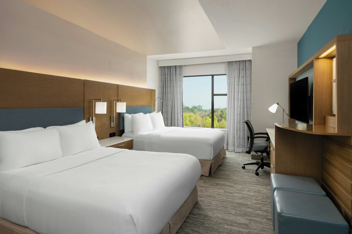 Une chambre d’hôtel avec deux lits, un bureau, une chaise, une télévision et une grande fenêtre donnant sur un beau paysage.