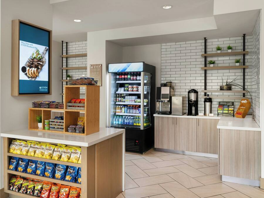 A clean, modern kitchen area with a vending machine stocked with beverages, snack shelves, and a digital menu display.