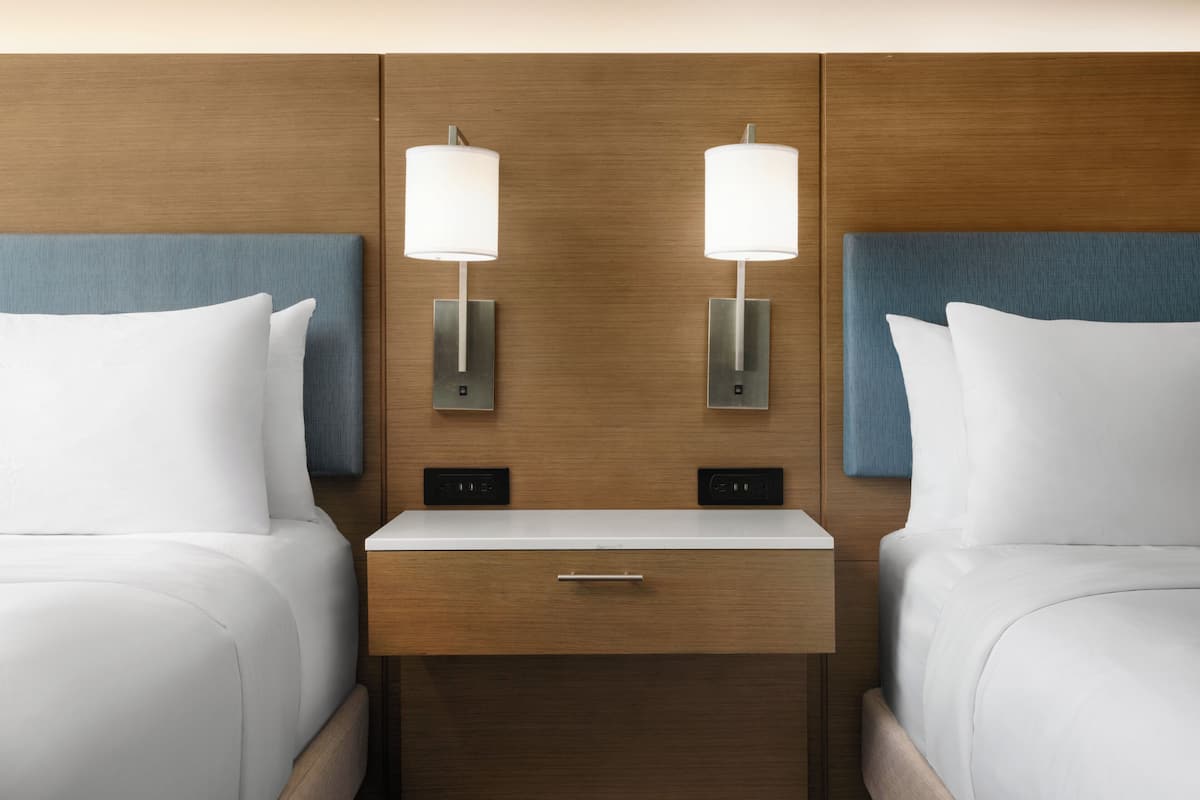 Een hotelkamer met twee bedden, een nachtkastje met lade en wandlampen.