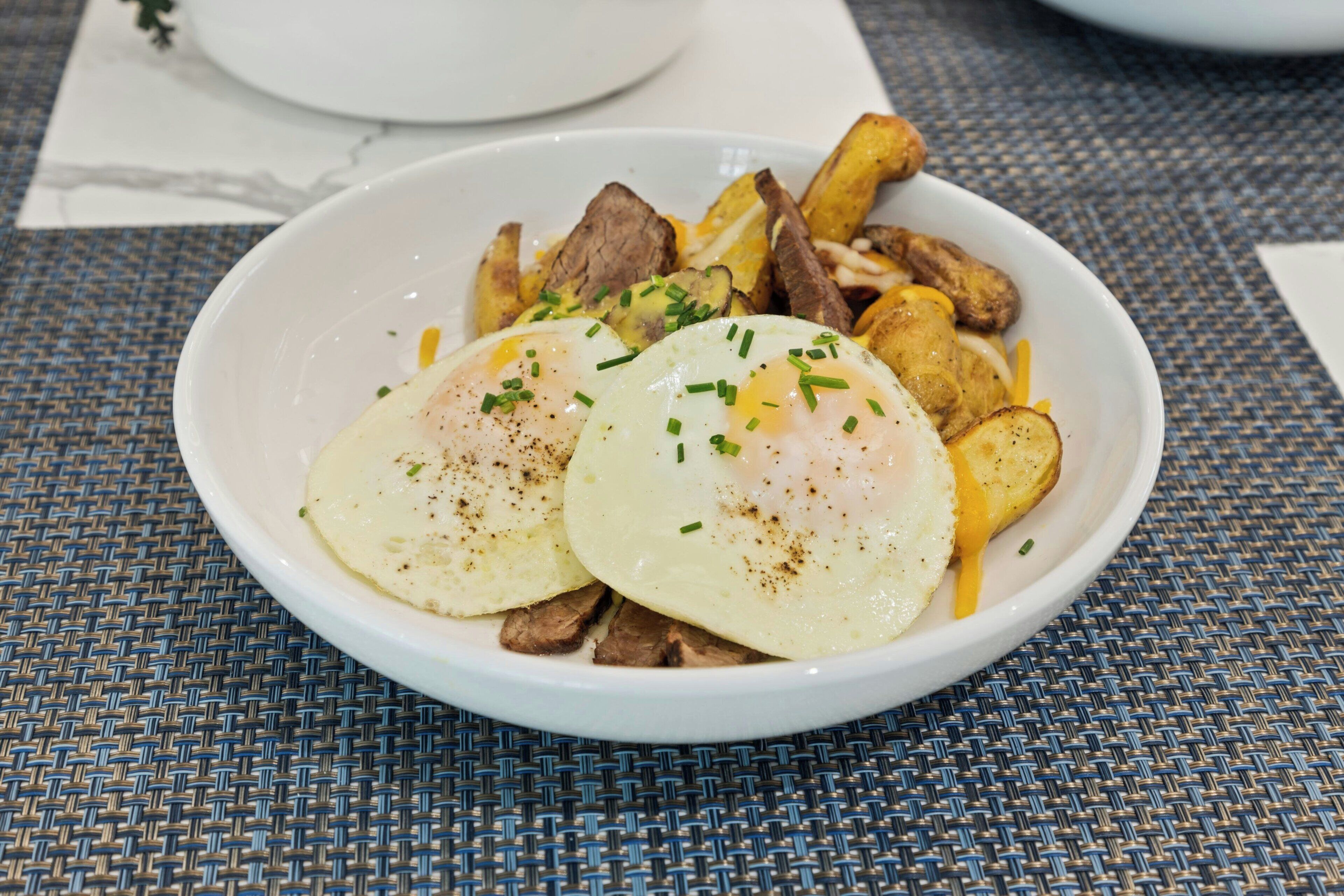 A bowl of food with eggs, potatoes, and meat.
