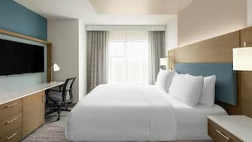 A hotel room with a bed, desk, chair, TV, and a window with curtains.