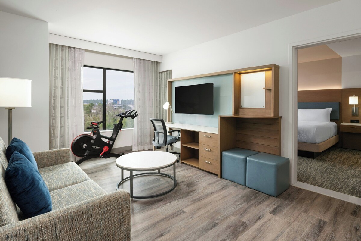 Une chambre d’hôtel équipée d’un lit, d’un bureau, d’une chaise, d’une télévision et d’un tapis de course, et offrant une vue sur la ville.