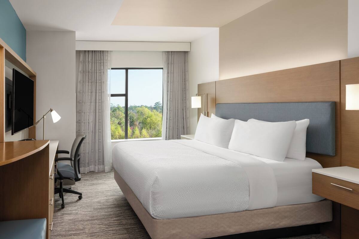 Een hotelkamer met een groot bed, een bureau met stoel, een televisie en een raam met gordijnen.