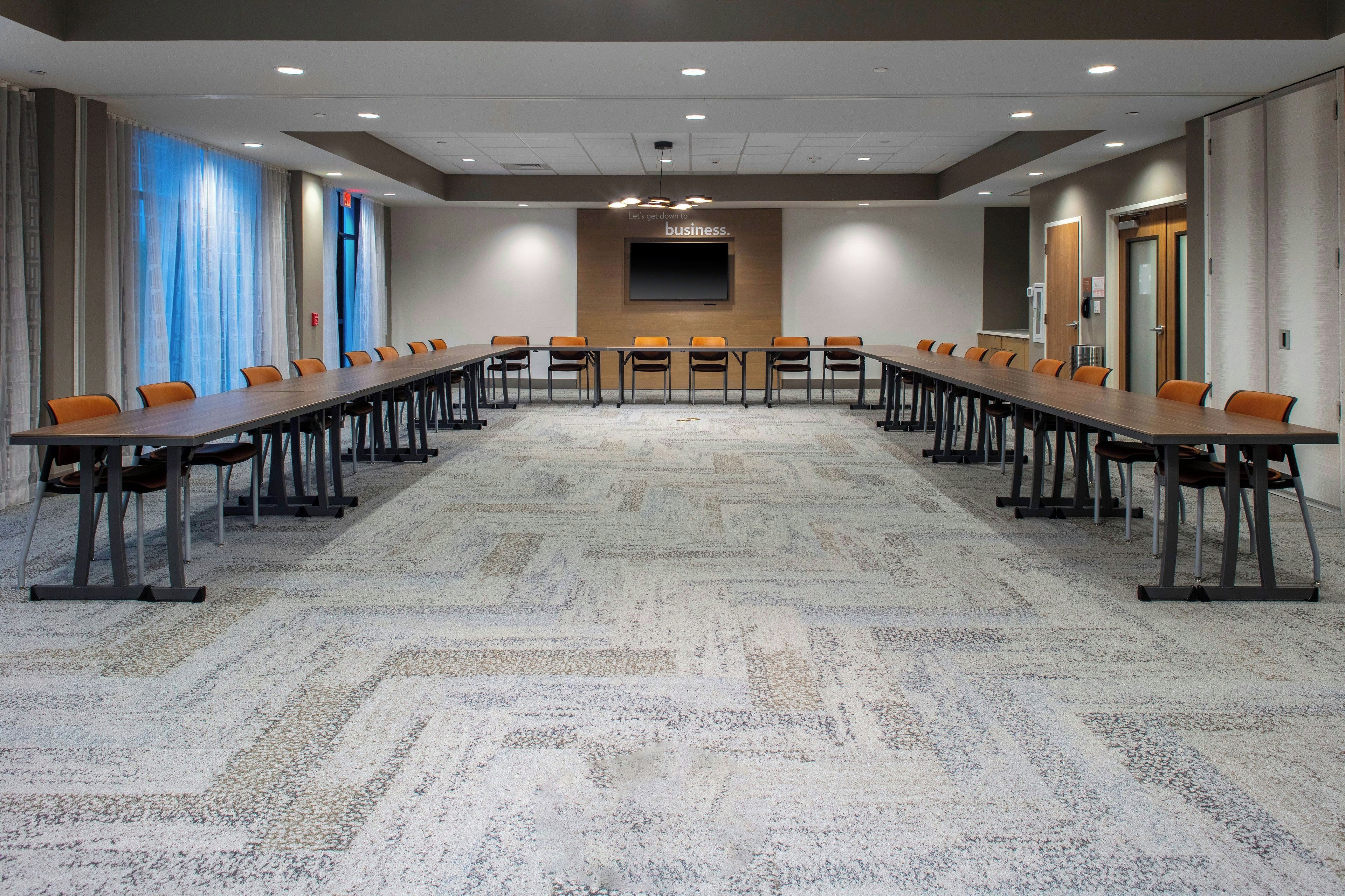 Un salón de conferencias con una larga mesa, sillas, una pantalla y suelo alfombrado.