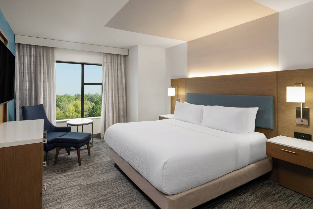 Hotelkamer met een groot bed, een bureau, een stoel, een klein tafeltje en een raam met gordijnen.