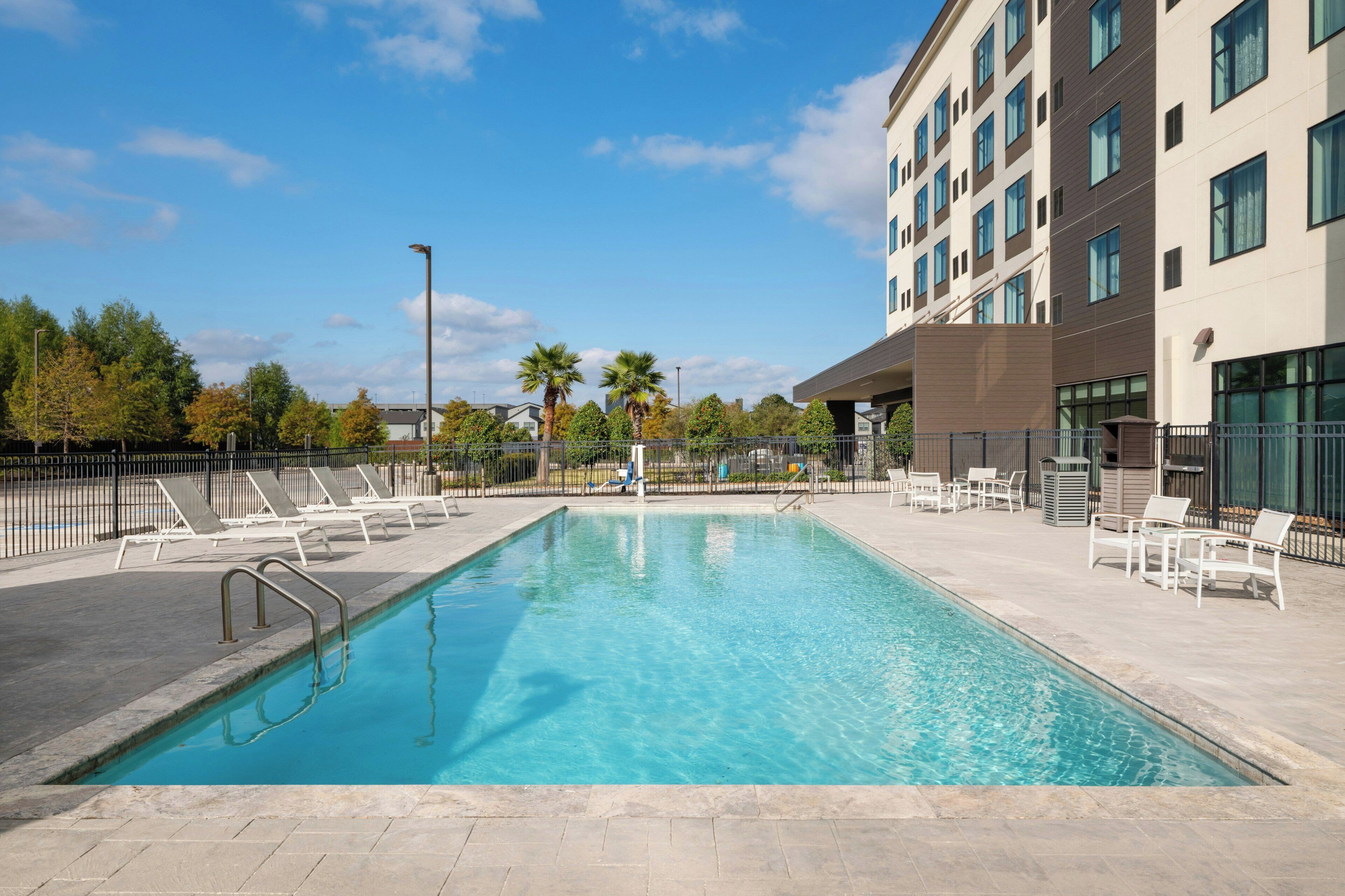 A rectangular swimming pool with clear blue water, surrounded by a paved deck.