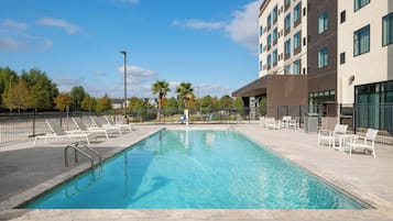 A rectangular swimming pool with clear blue water, surrounded by a paved deck.