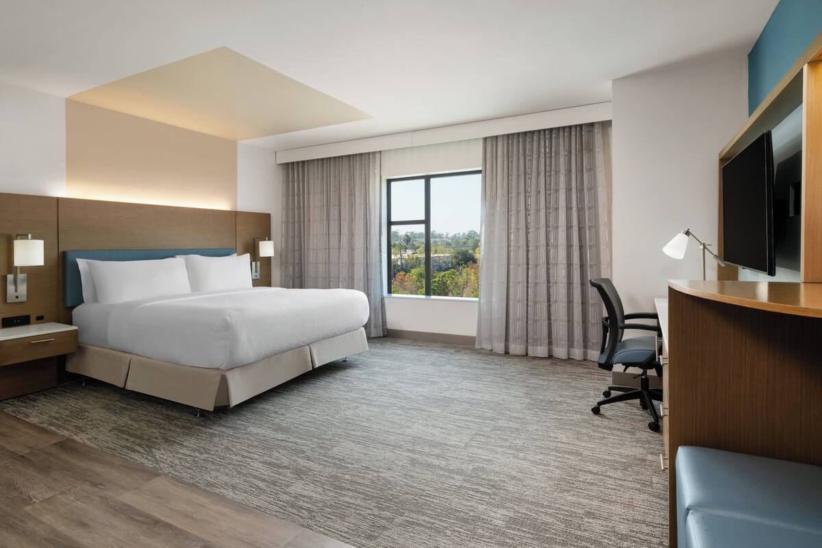 Een hotelkamer met een bed, bureau, stoel, televisie en groot raam.