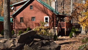 A log cabin with a green roof, a wooden deck, and a stone chimney. - RIVERFRONT 2 STORY, 4 BR, 2 Bath, Washer/Dryer, HOT TUB, Pet Friendly (Elkins)