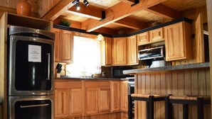 A kitchen with wooden cabinets, a stainless steel refrigerator, and a bar stool. - RIVERFRONT 2 STORY, 4 BR, 2 Bath, Washer/Dryer, HOT TUB, Pet Friendly (Elkins)
