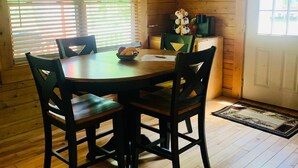 A wooden cabin interior with a round dining table, four chairs, a window with blinds, and a door. - RIVERFRONT 2 STORY, 4 BR, 2 Bath, Washer/Dryer, HOT TUB, Pet Friendly (Elkins)