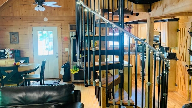 A cozy log cabin interior with a spiral staircase, leather sofas, and a dining area. - RIVERFRONT 2 STORY, 4 BR, 2 Bath, Washer/Dryer, HOT TUB, Pet Friendly (Elkins)