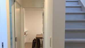 A hallway with a staircase leading to a landing. There is a wooden table with chairs and a small shelf with items on it. - Bella Corner (Furano)
