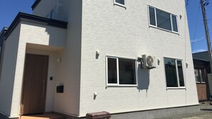 Un bâtiment à deux étages, à l’extérieur blanc, avec une porte d’entrée et un petit porche.