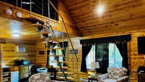 Ein gemütliches Blockhaus-Interieur mit Wendeltreppe, Holzwänden und zwei gemusterten Sesseln.