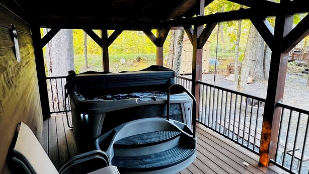 Ein überdachter Außenbereich mit Whirlpool und Stühlen, umgeben von einer Holzterrasse und einem Geländer.