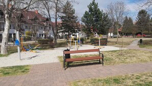 A park with a paved walkway, a wooden bench, exercise equipment, and trees. - Holiday home with garden and terrace near the center (Siófok)