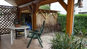 A covered patio area with a table and chairs, surrounded by potted plants and a wooden fence. - Holiday home with garden and terrace near the center (Siófok)