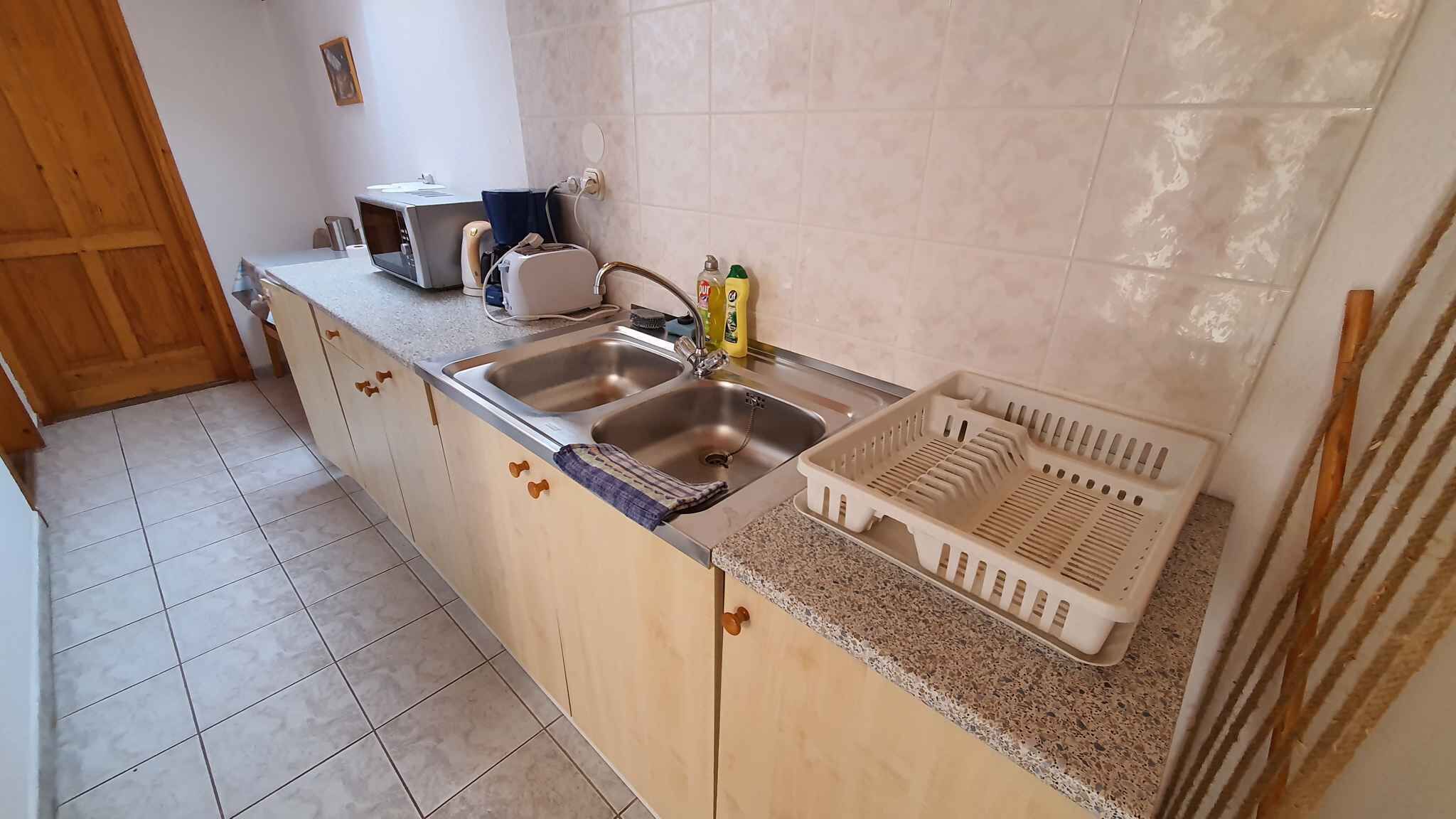 A kitchen with a double sink, a microwave, and a toaster. There is a dish rack and cleaning supplies on the counter.