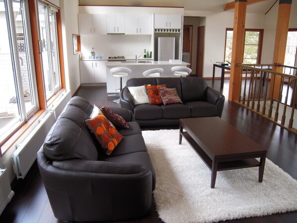 A modern living room with a sofa and a coffee table, a kitchen in the background, and a staircase leading to another level.